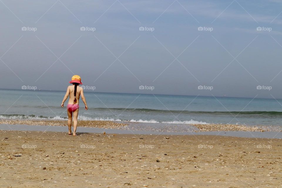 Girl with pink yellow hat walking on sea shore 