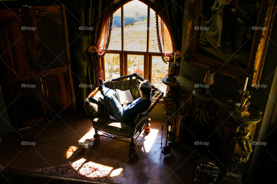 Reading is a big part of my daily routine. Image of woman sitting by window light reading a book with a cup of coffee.