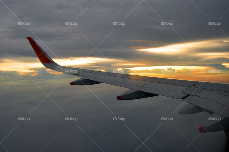 Airplane wing in evening sky look through the window, clouds are yellow by sunlight of sunset