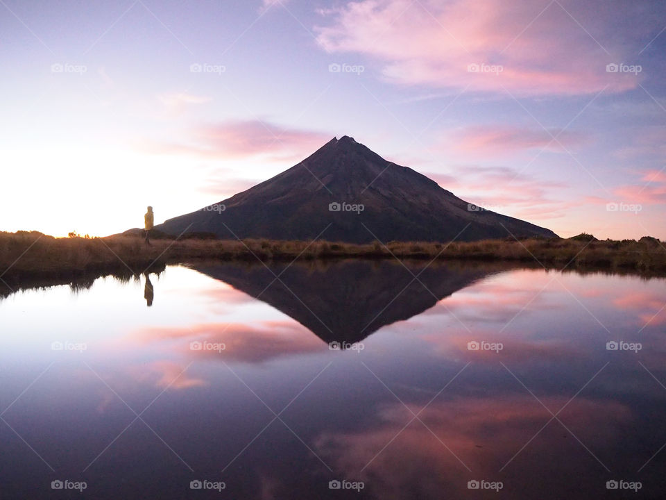 A girl and the mountain are reflected perfectly on the surface of the still lake