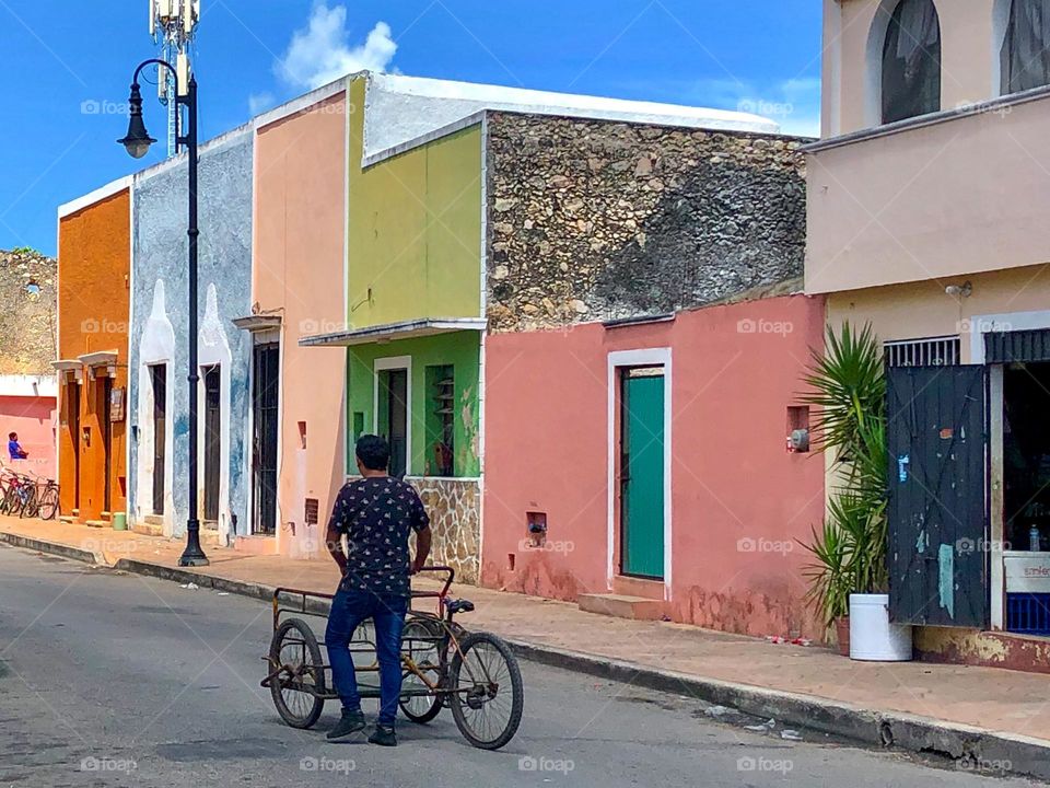 A man walks his bicycle - which serves as a transporter - down a colorful Mexican street