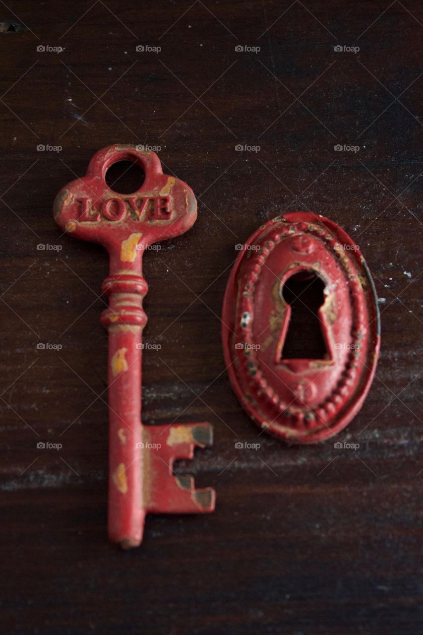 Red rustic vintage key with the word “LOVE” and keyhole on dark wooden surface