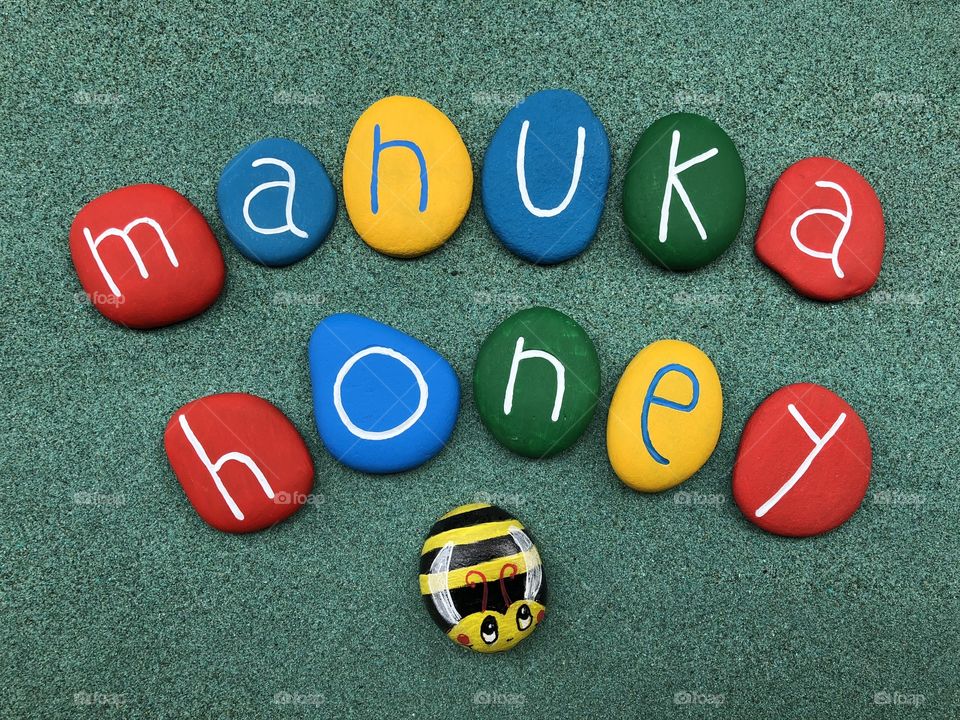 Manuka Honey text with multicolored stones with a bee design over green sand