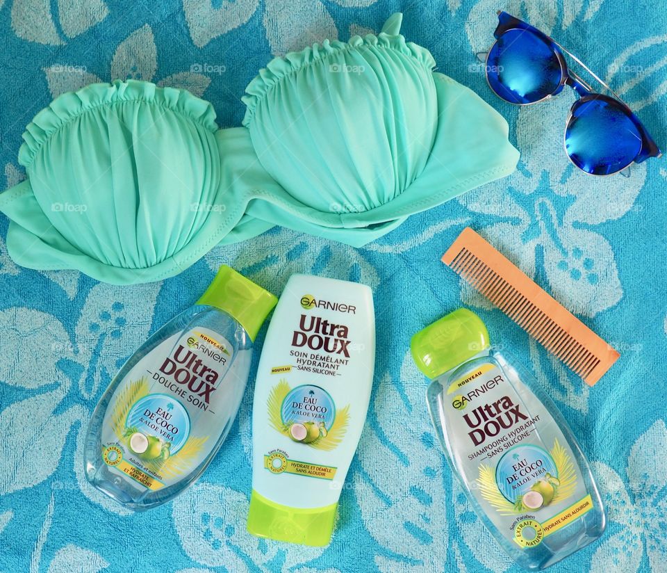 Garnier eau de coco shampoo, conditioner and bath gel on a blue towel with comb and bikini.