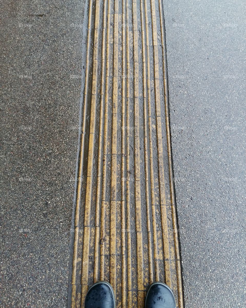 Grey asphalt with a yellow center line and a pair of selfie rain boots