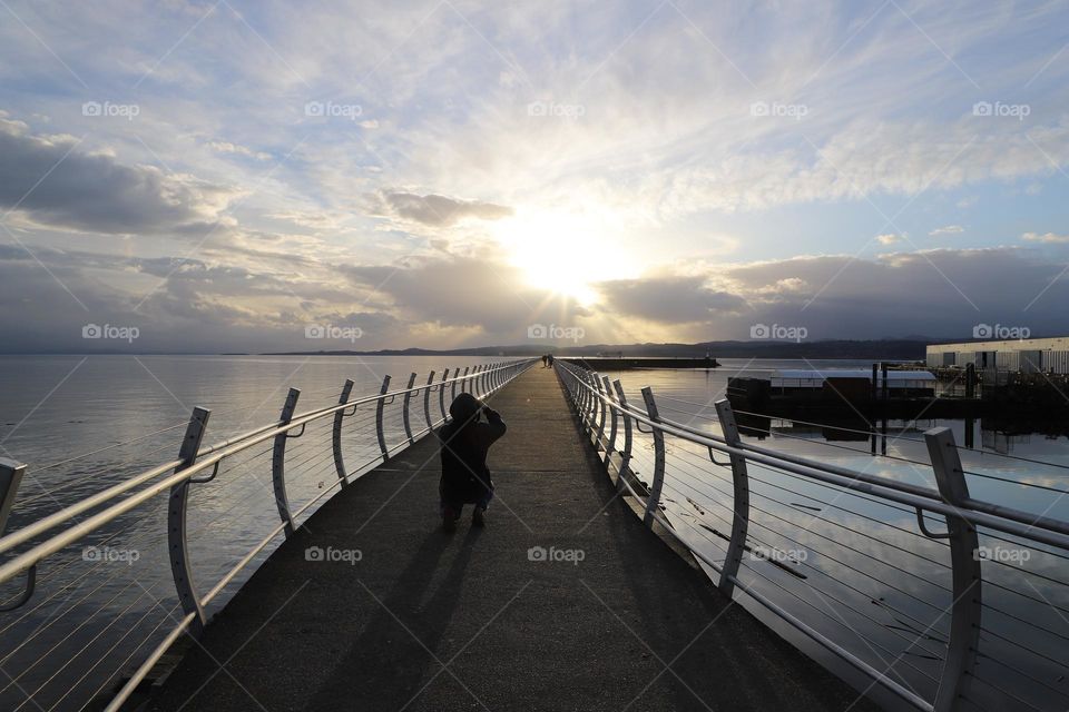 Silhouette of a man capturing the sunset at the end of the breakwater 