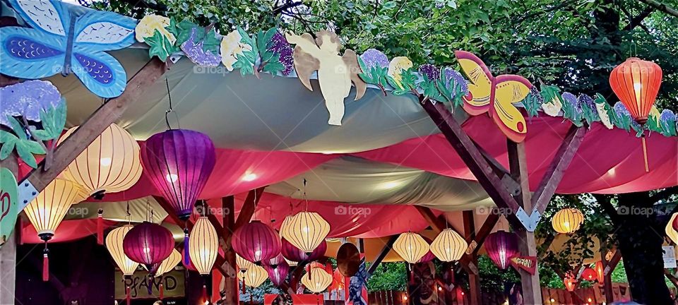 Paper lanterns adorn the ceilings of various stands at the “Tollwood” summer festival in “Munich”, Bavaria that presents music as well as a market for folklore fare, arts and crafts and merchandise from around the World. 2024. Hypnotic Productions