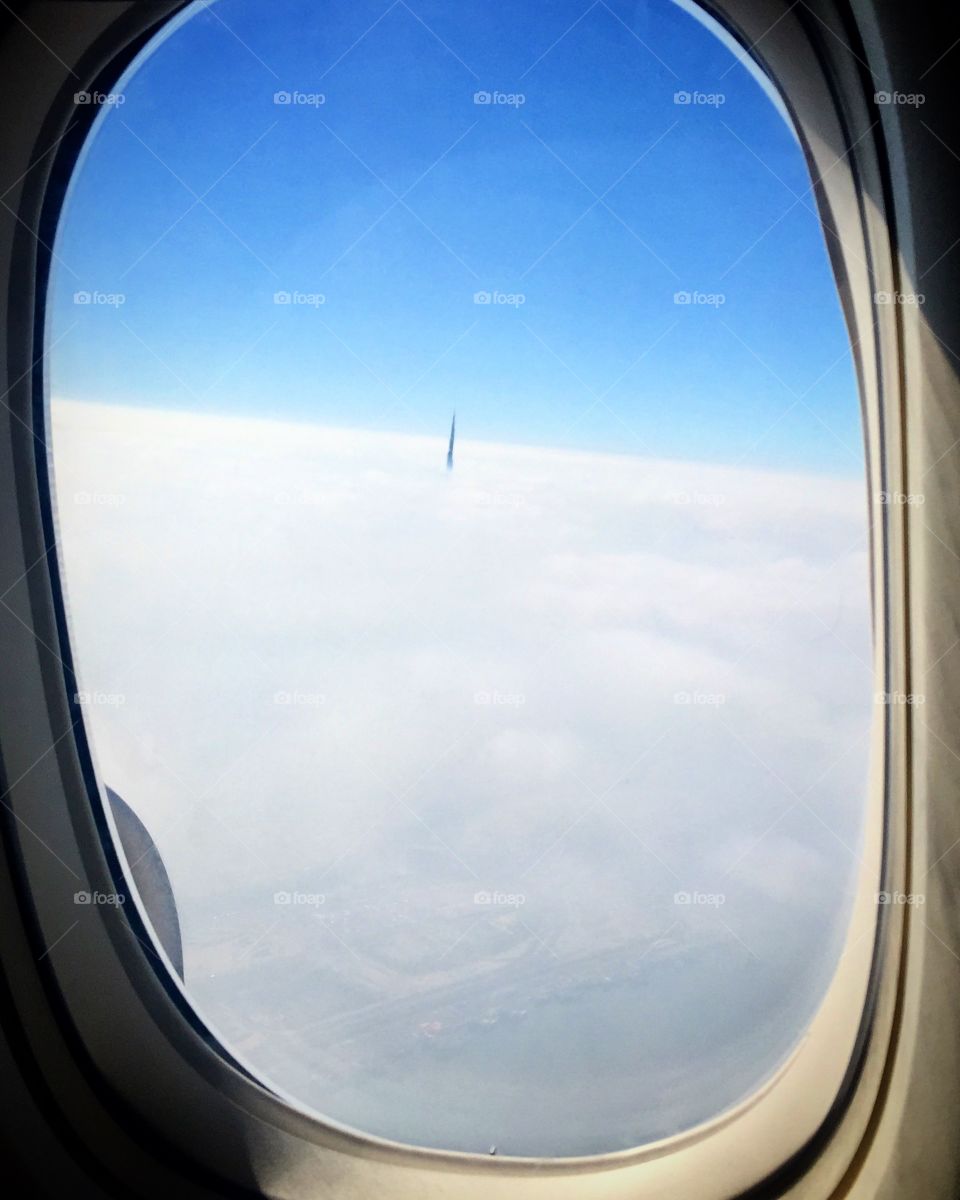 Tip of the tallest building in the world, Burj Khalifa Dubai peaking through clouds seen from airplane window 