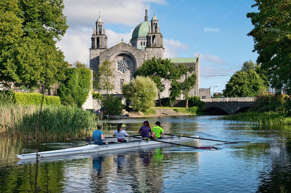 Group of girls rowing in river corrib in front of Galway cathedral in Ireland