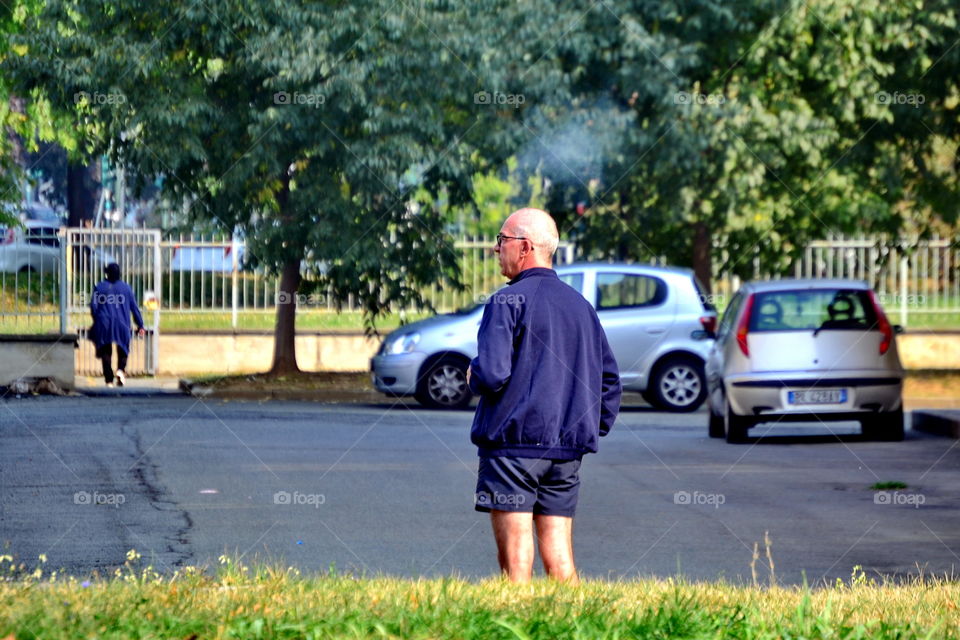 an elderly man in shorts, smoking a cigarette outdoors