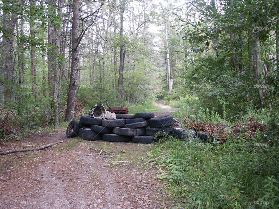 Tires stacked to block this back road. Can't get through tires blocking back road in woodland!