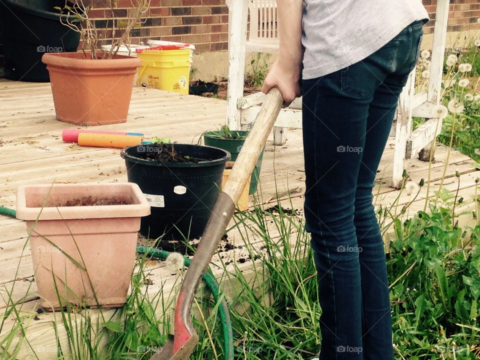 Teen planting on a deck. Tiny teen holding shovel with pots all around