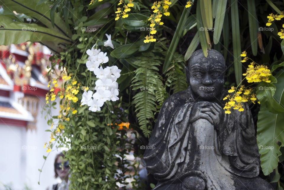 Stone statue - surrounded by greenery and flowers - in a Bangkok palace - combination of simplicity and extravagance.