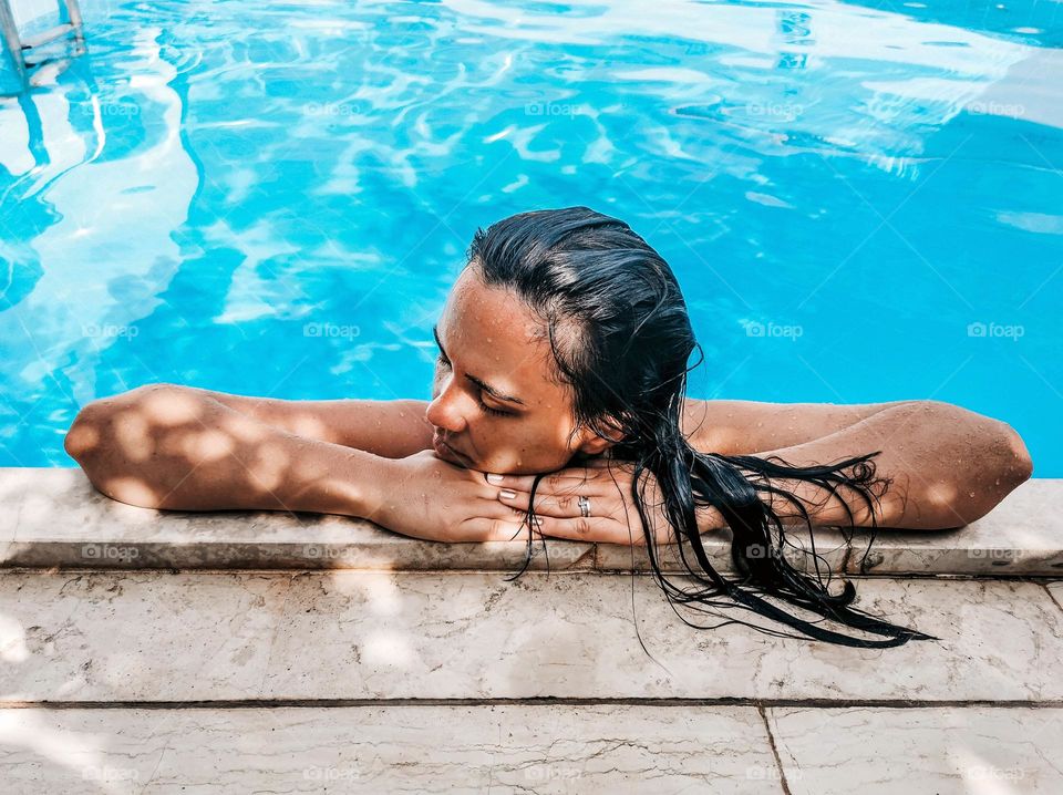 Young woman with wet dark hair relaxing on edge of swimming pool