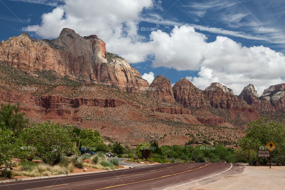 Red mountains and cloudy sky. Mountainous scenery close to Zion National Park in Utah, USA. Partly cloudy sky. Red, paved road lead view to mountains.