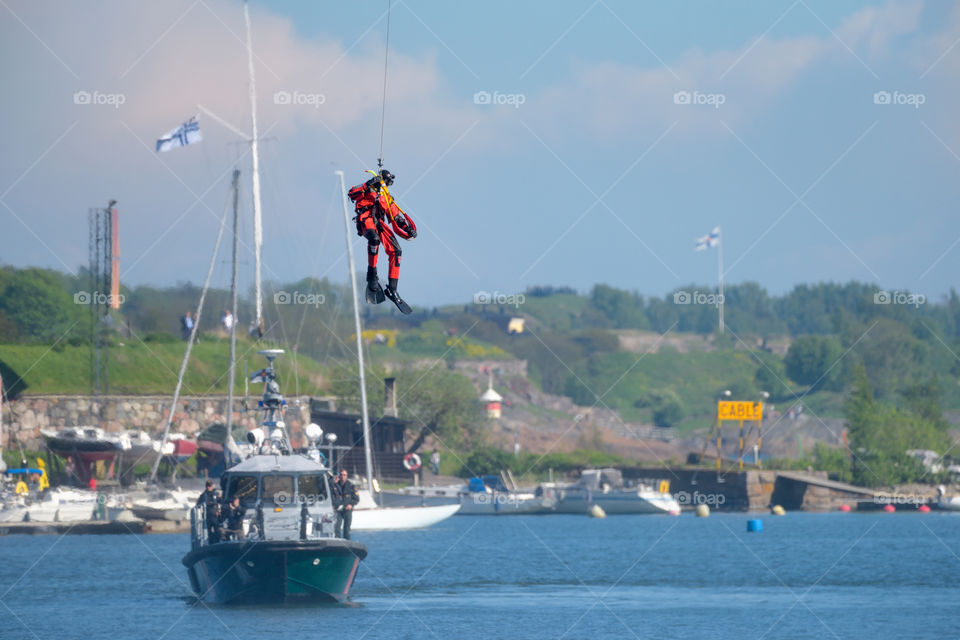 Helsinki, Finland - June 9, 2017: Unidentified Finnish Coast Guard rescue swimmer drops down to the Baltic Sea be a wire in rescue exercise or performance in the Kaivopuisto Air Show 2017 in front of Suomenlinna fortress island with small Coast Guard