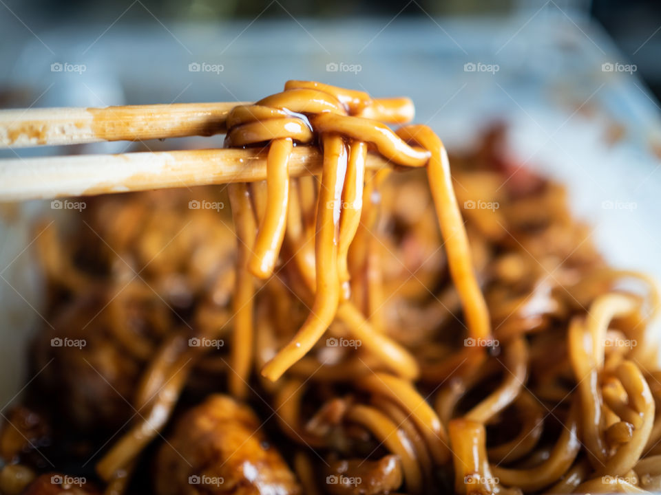 Teriyaki noodles with chicken being eaten with wooden chopsticks 