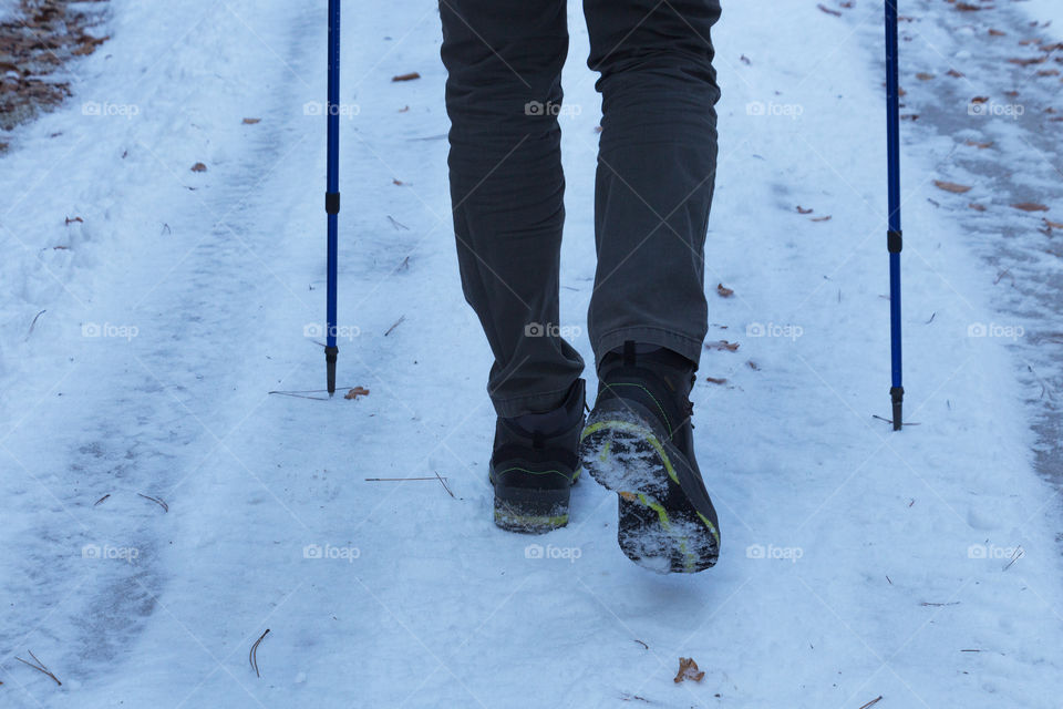 Feet of walking man in the snow with winter leather boots and walking sticks