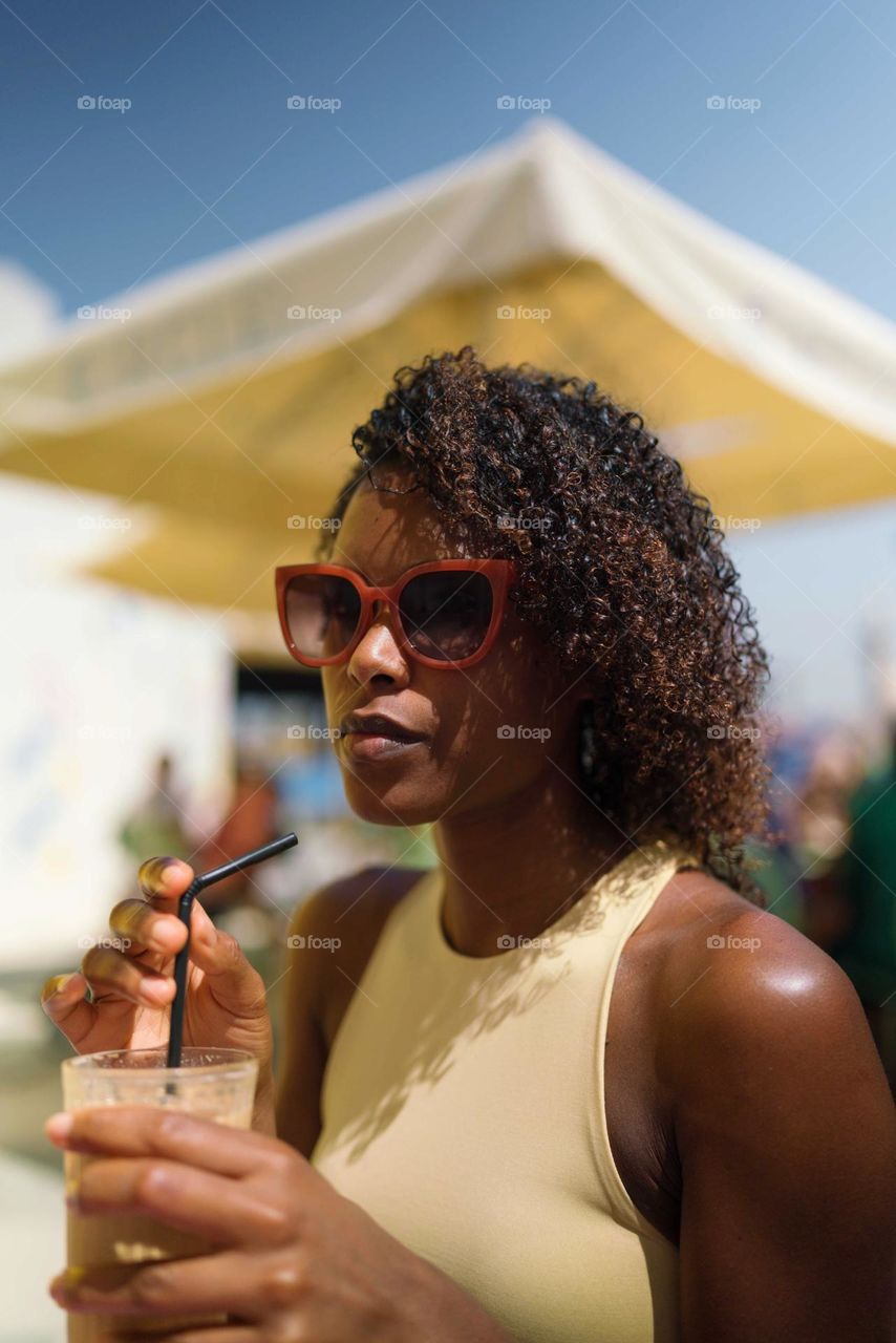 Beautiful black woman with Afro hair having iced coffee for breakfast in the outdoor cafe