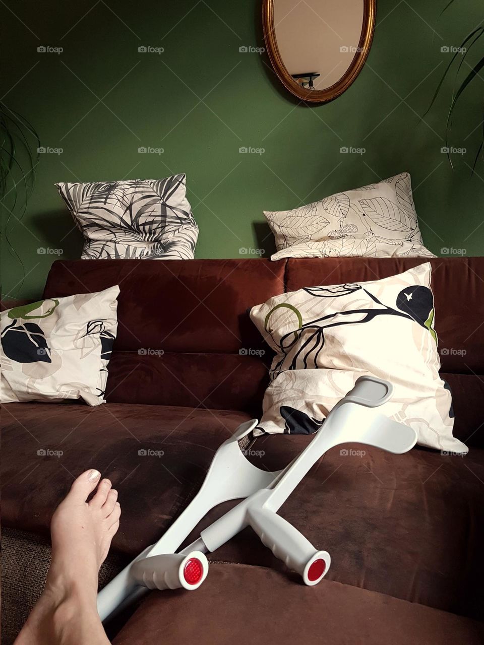 View of crutches on a sofa next to a foot without stocking and shoe