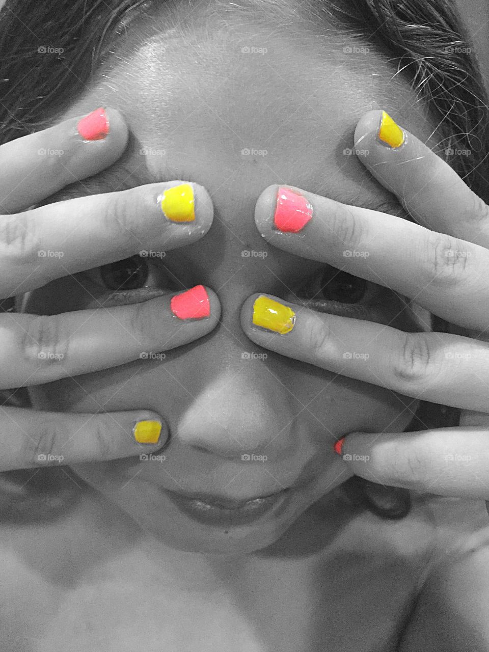 Young girl with pink and yellow painted finger nails. Black and white photo with color effect. 
