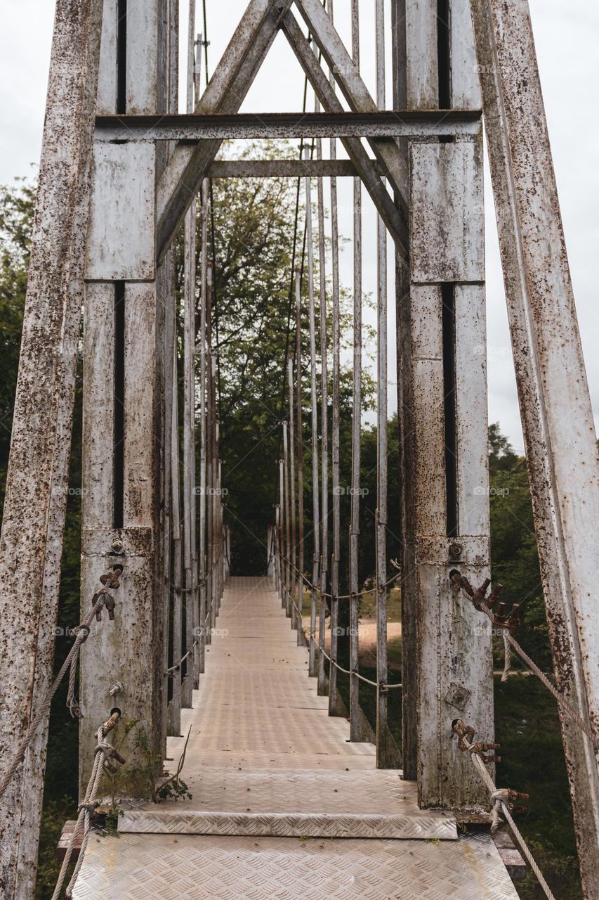 A hanging bridge made from steel. Long, old steel bridge with beams, cables and sheets.