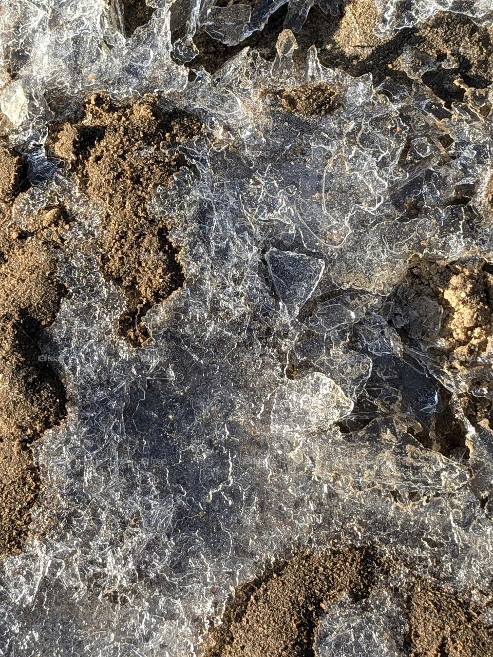 A close-up of a sheet of ice with small cracks due to the texture of the sand it's covering. A cold, November morning. Juxtaposition in nature.