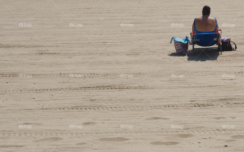 A rear view of a woman seated and relaxing at the beach on a summer day.