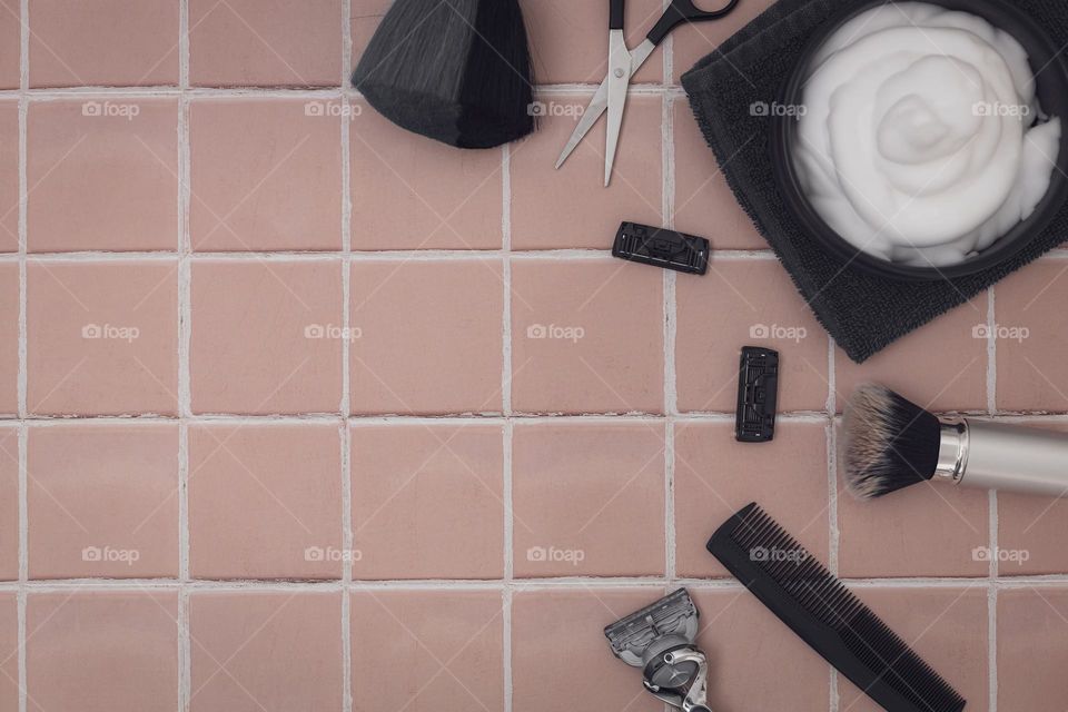 A porcelain cup with shaving foam on a terry napkin with scissors, a comb and a razor, razor heads lie in a circle on the right on a brown natural tiled background with copy space on the left, flat lay close-up. The concept of a man barbershop, man