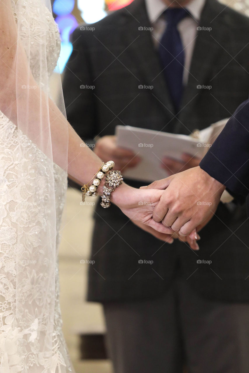 Bride and groom Holding hands during wedding ceremony while pastor reads vows