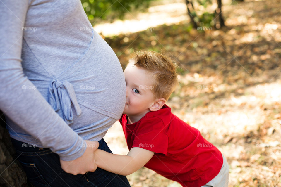 Small boy kissing belly of his pregnant mother