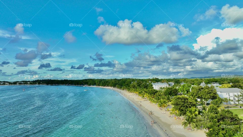 A Birds Eye view of the turquoise sea kisses the long stretch of pristine white sand, fringed by lush green palm trees along seven miles beach in Negril Jamaica
