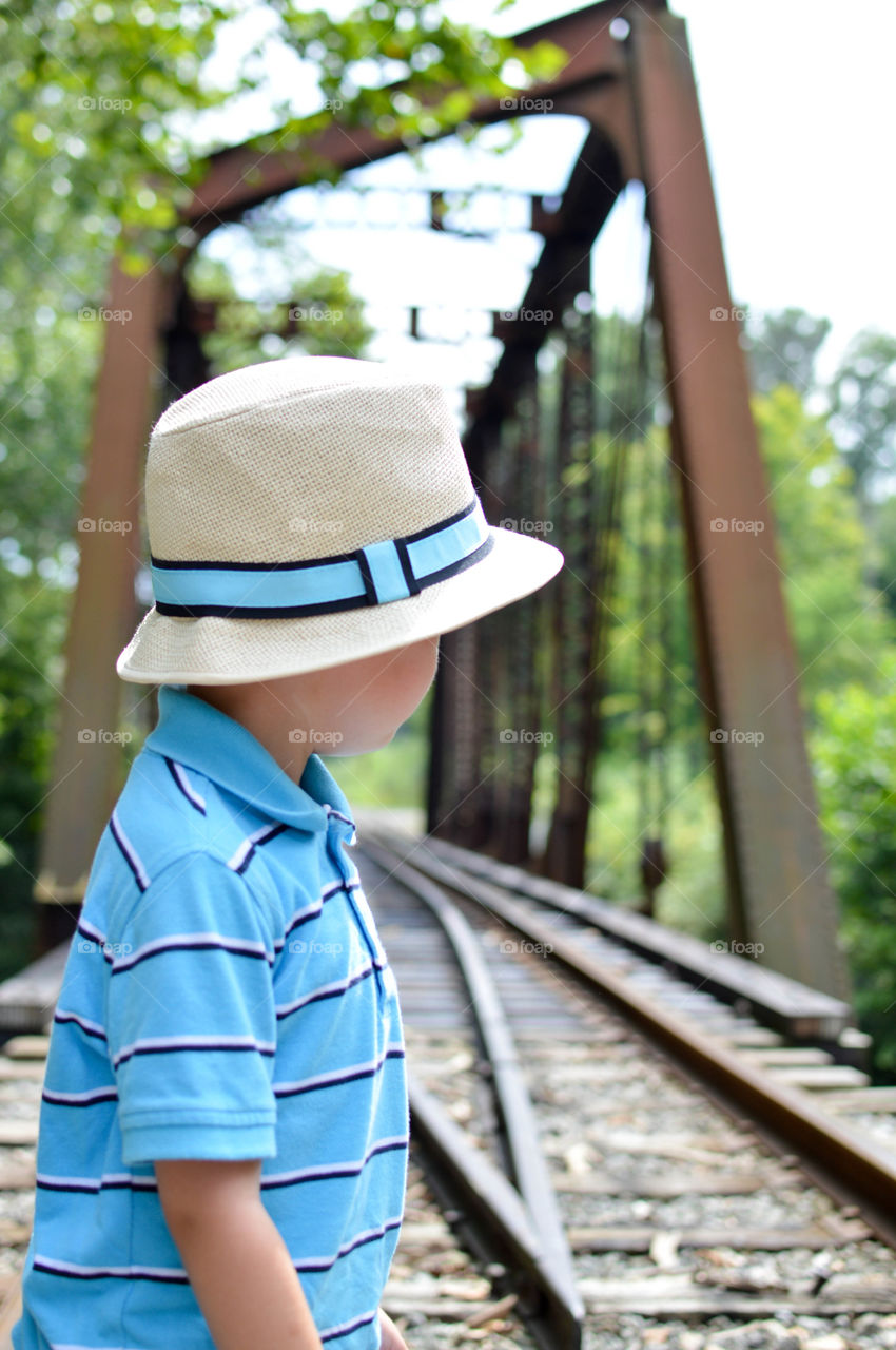 Young boy wearing a hat and looking back while standing on a railroad bridge