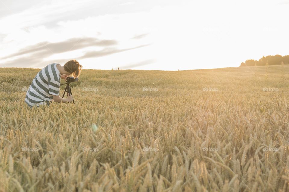 a teenager photographs a sunset in a wheat field on a phone camera that is mounted on a tripod