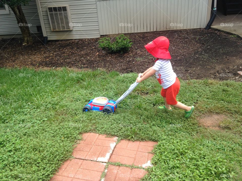 Toddler boy mowing the lawn.