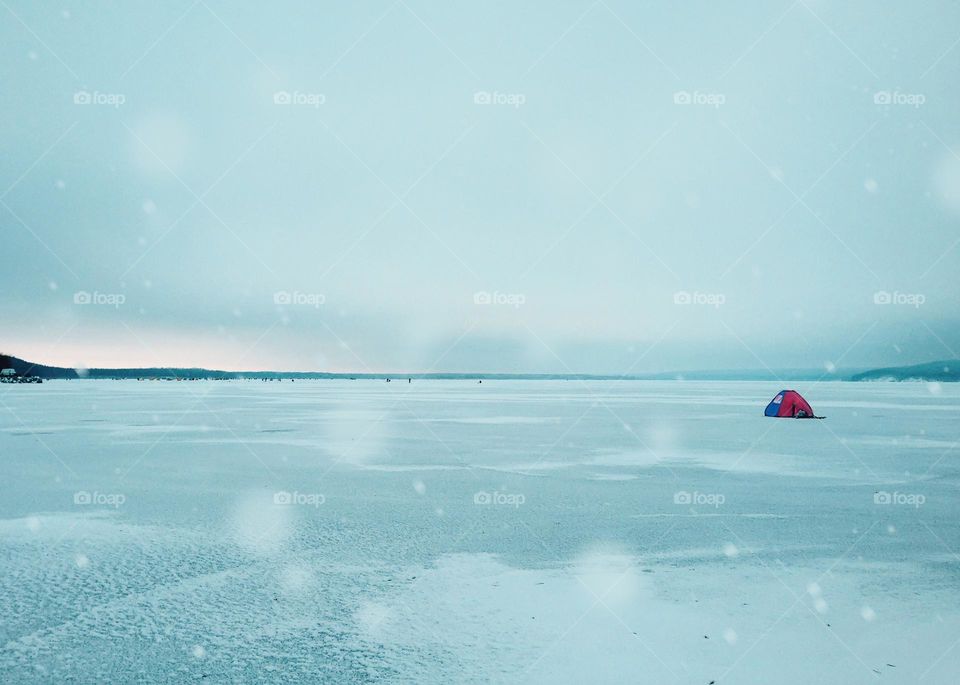 Tiny red fisherman tent on frozen lake 