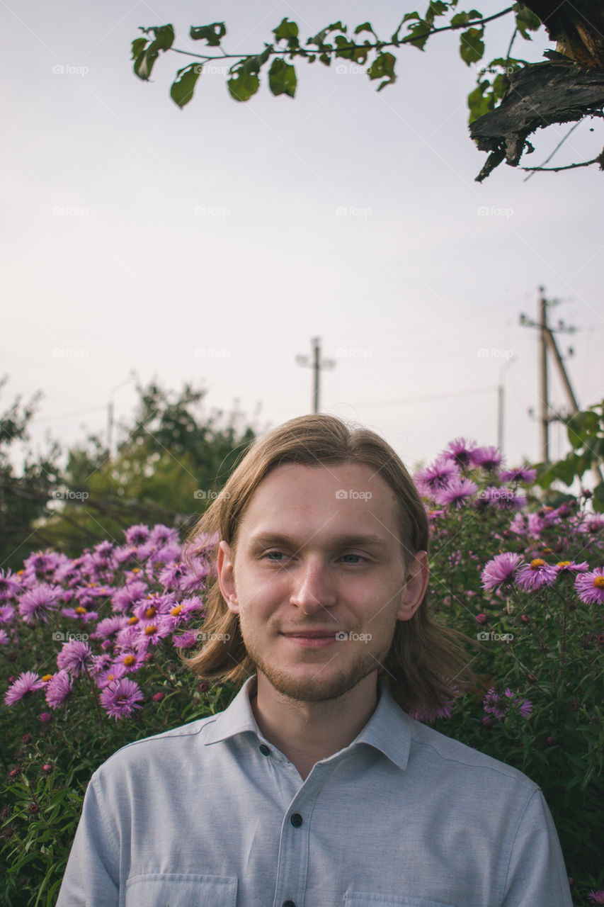 Portrait of a cute guy in the garden with a purple flowers on the background. Late summer, countryside.