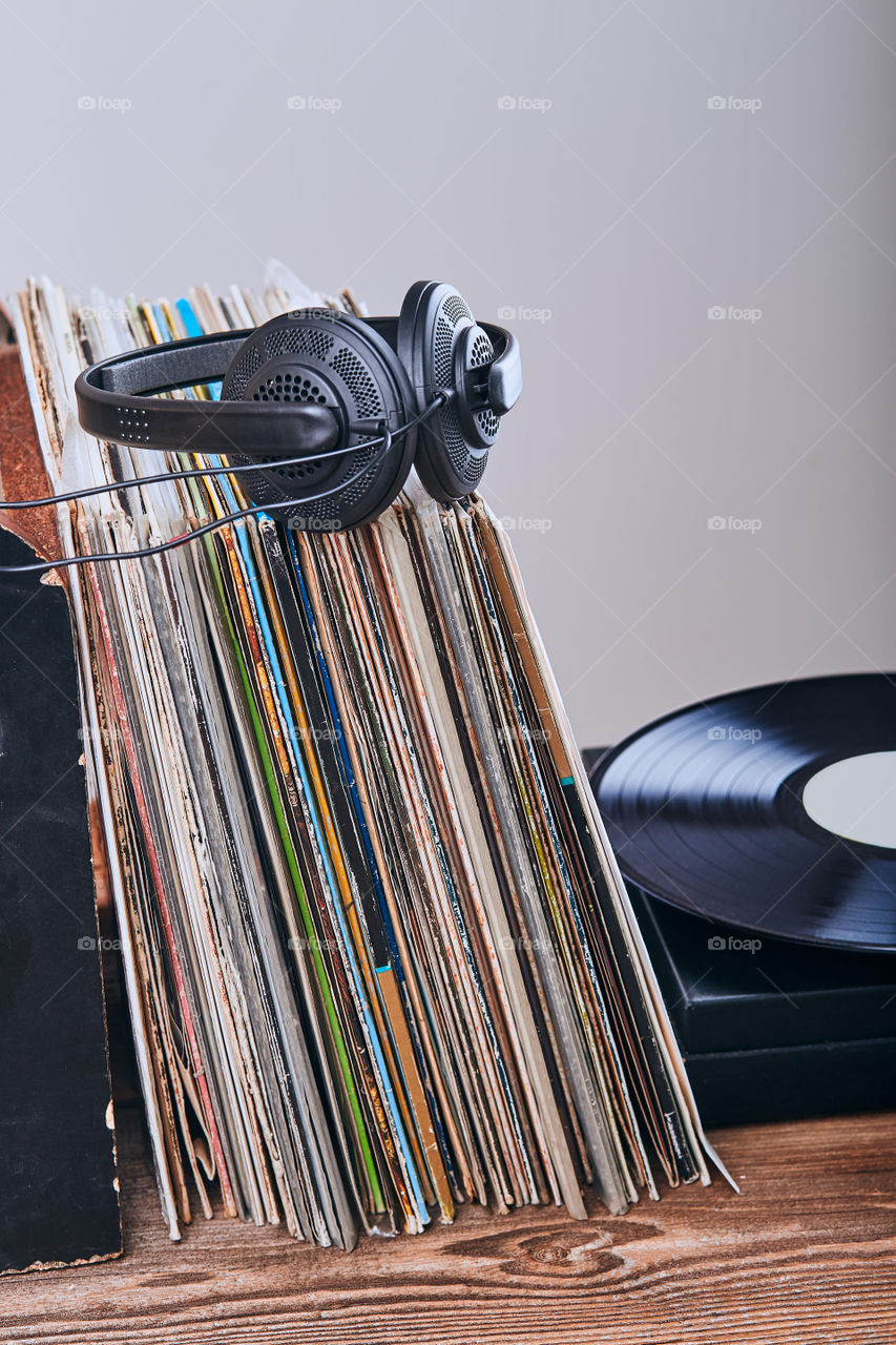 Stack of many black vinyl records, turntable vinyl player and headphones put on the stack. Classic stereo set. Candid people, real moments, authentic situations