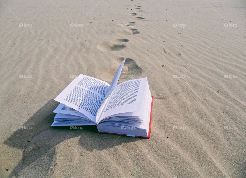 an open book lies on a sandy beach