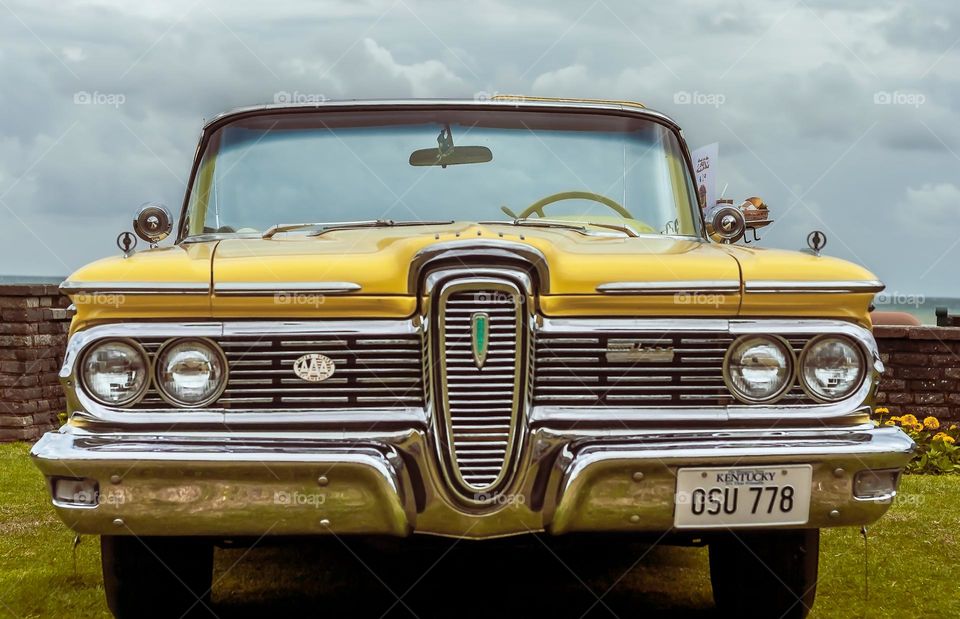 A bright yellow Haas 1950s convertible complete with diner tray on the side, against a blue and cloudy sky