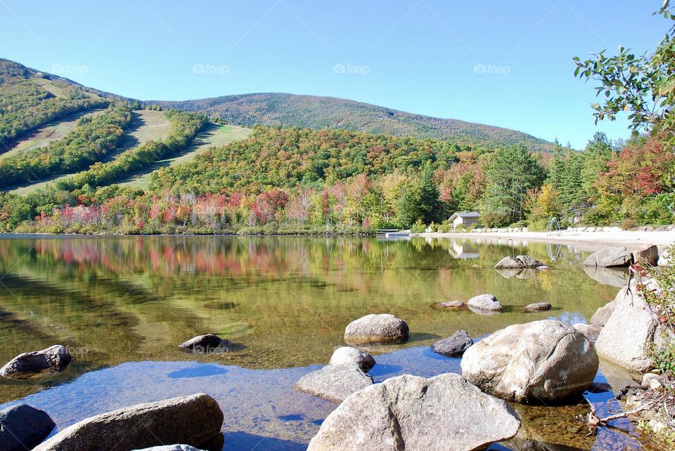 Mountains in the fall with ski runs visible amongst the trees and a lake in the foreground 