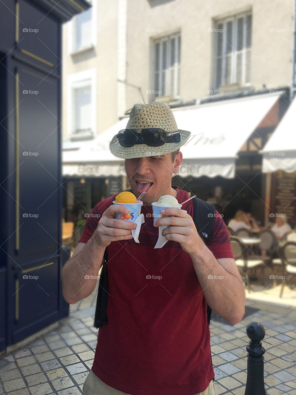 Young man in straw hat eats two ice creams at summer day