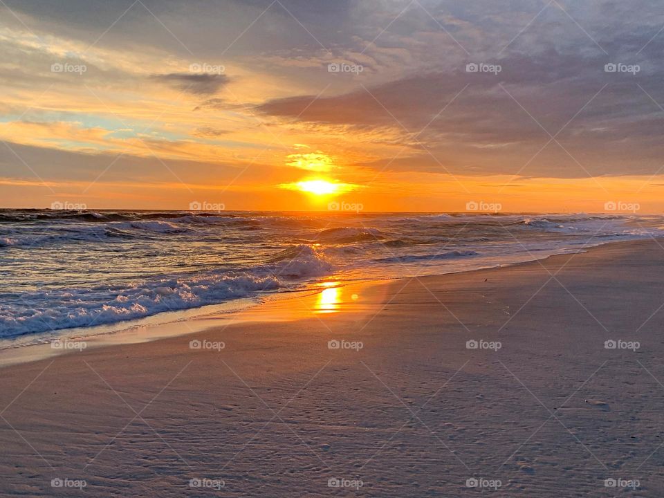 The color of twilight and sunset. The dramatic hurried rush of yellow and orange collapse as the sun sank below the gorgeous, cloudy skyline. White sand on the beach 