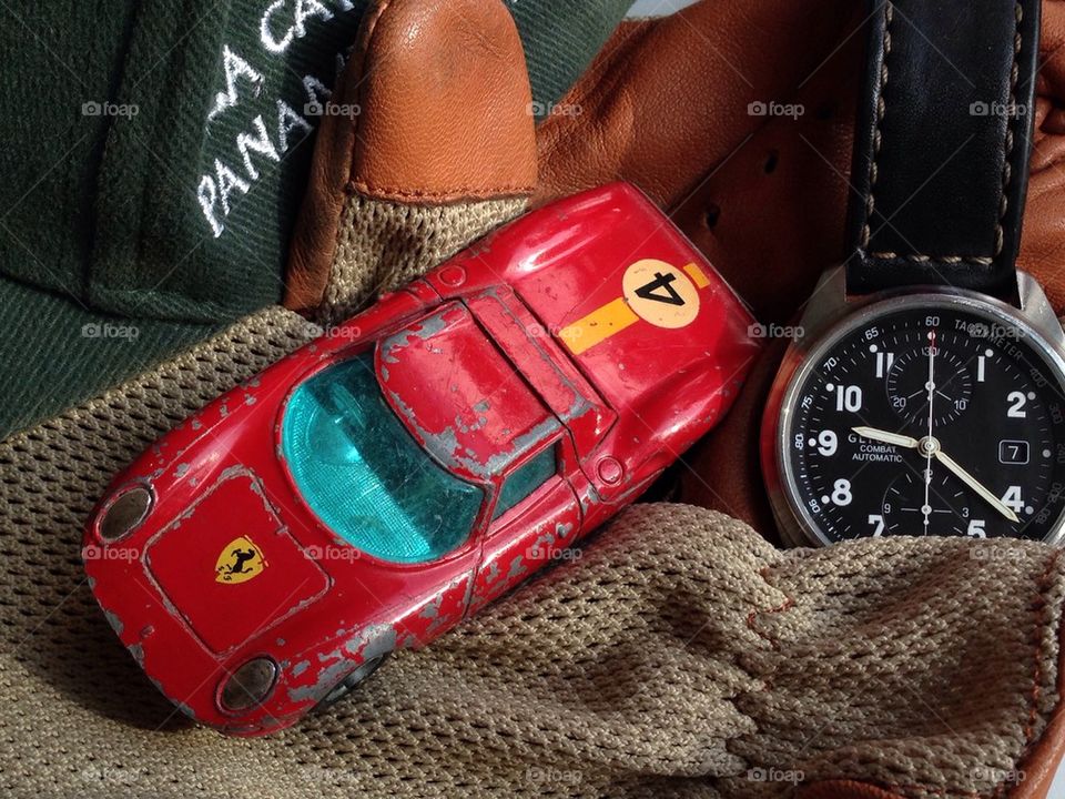 Ferrari 275 LM model sitting with a pair of driving gloves and a chronograph watch