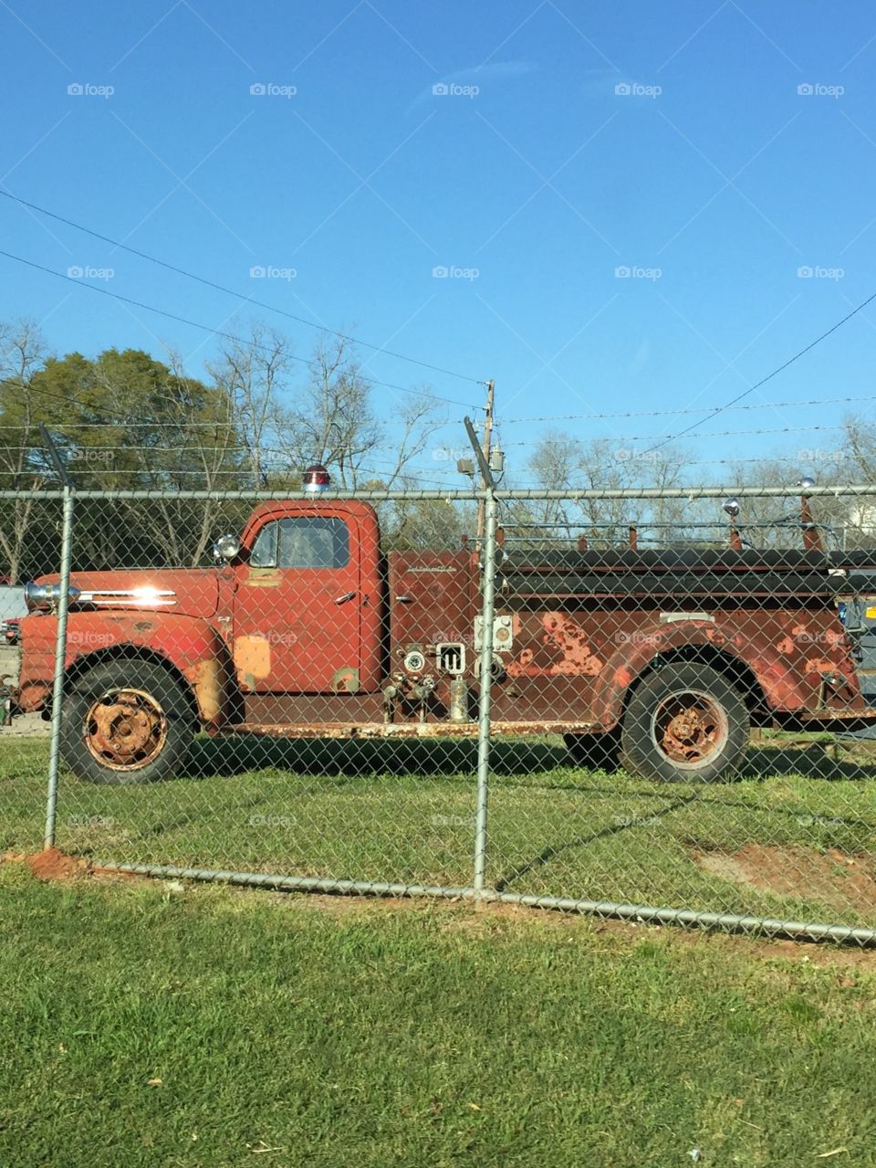 Very old , faded red, rusty fire truck behind fence.