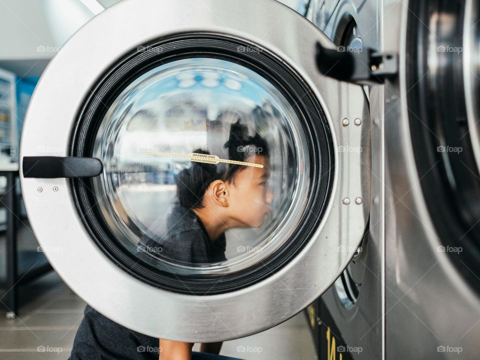A boy looking into a washing machine in a laundrette