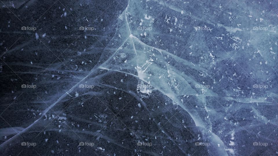 Dark blue full of bubbles cracked pond ice.