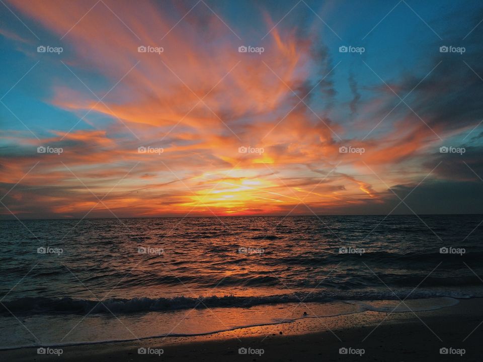 Beautiful fiery sunset over the ocean. . Swirling clouds lit up by perfect sunset over Gulf of Mexico. 