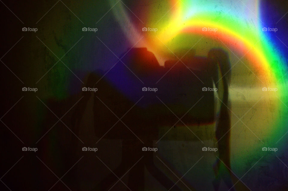 A bright rainbow contrasts to the dark shadow of a photocamera and the darkness of the room, magical ambiance.