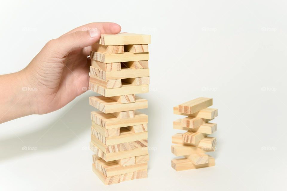 Jenga game isolated on white background. The child builds a tower from wooden blocks
